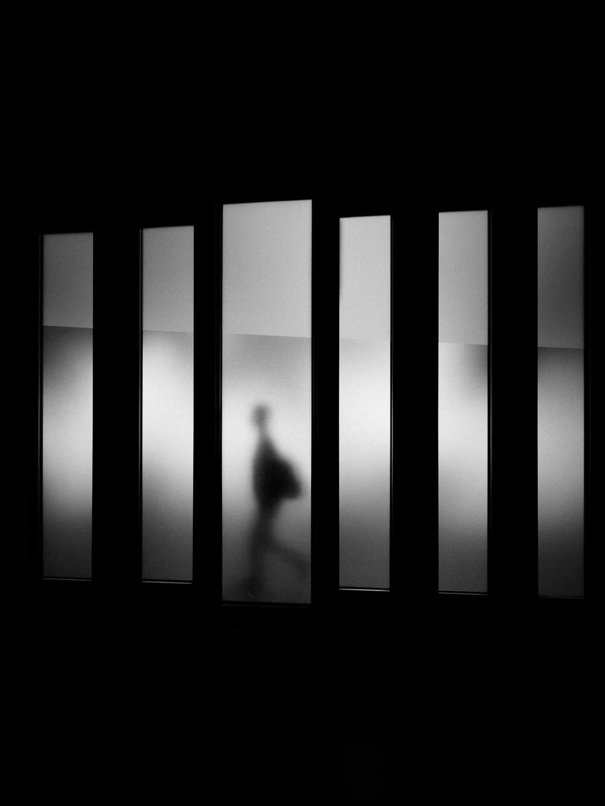 A figure passing tall lit panels in a dark corridor